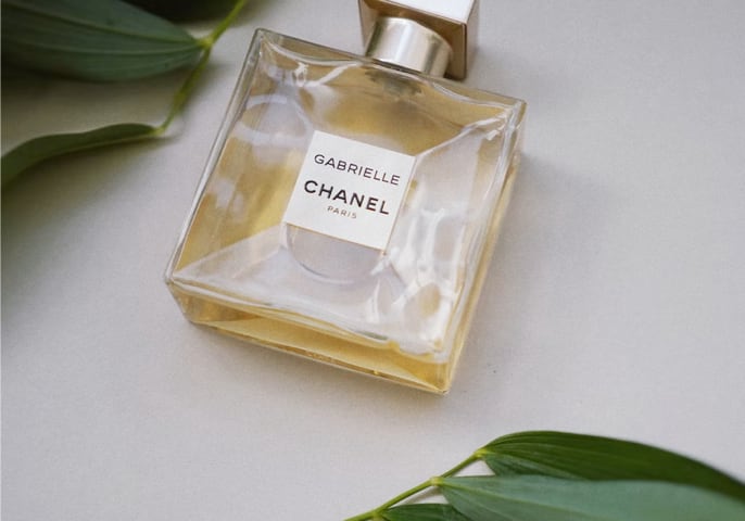 Gabrielle Chanel perfume bottle alongside leaves on either corner